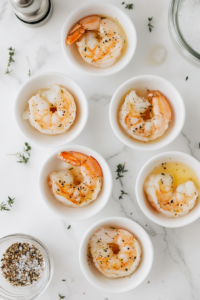 This image shows shrimp being seasoned with salt and freshly ground black pepper, enhancing the dish’s depth of flavor.