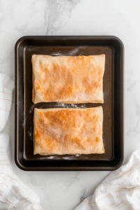 This image shows crescent dough sheets being stacked and gently pressed together to seal in the cinnamon-sugar filling before cutting and twisting.