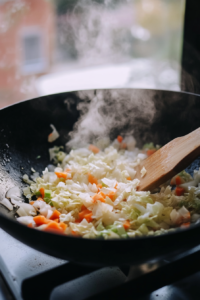 This image shows garlic, ginger, and vegetables sizzling in a wok, releasing their aroma and building layers of flavor.
