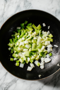 This image shows celery stalks and onions being stir-fried in a pan, adding flavor and texture to the Black Pepper Chicken dish.