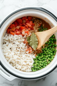This image shows diced tomatoes, green peas, and rich chicken stock being mixed into the slow cooker, creating a flavorful and hearty rice mixture.
