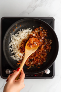 This image shows freshly minced garlic being added to a pan with sautéed onions, infusing the dish with a rich aroma and depth of flavor.