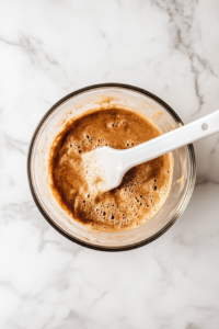 This image shows dry and wet ingredients being combined in a mixing bowl, forming a soft and thick banana bread cookie dough.