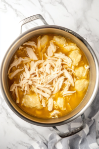 This image shows tender, shredded chicken being mixed into the pot of dumplings and broth, completing the dish.