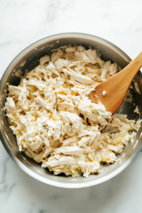 This image shows tender shredded chicken being mixed into the sautéed onions and melted cream cheese, creating a creamy and savory filling.