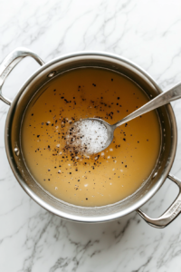 This image shows a spoon stirring a thickening agent, such as cornstarch or flour, into the simmering broth to create a hearty consistency.