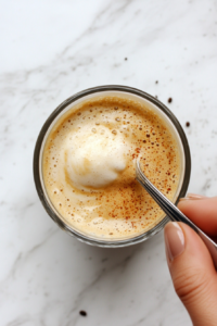 This image shows a spoon stirring the fluffy whipped coffee into the milk, blending the layers together for a rich and indulgent coffee treat.
