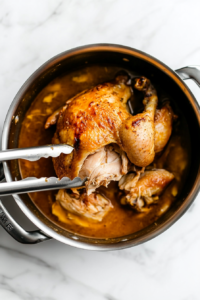This image shows a fine-mesh strainer being used to remove onions, celery, and other cooked vegetables from the broth, leaving a clear, flavorful liquid.