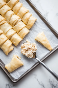 This image shows soft crescent roll dough being filled with the creamy chicken mixture and carefully rolled into neat, compact shapes.