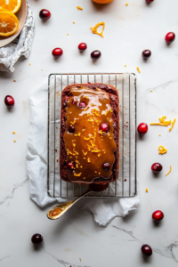 This image shows a rich, sweet orange glaze being drizzled over the cranberry orange loaf, enhancing its flavor before being sliced and served.