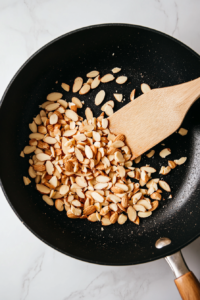 This image shows sliced almonds being toasted in a pan until golden brown, enhancing their nutty flavor and crisp texture.