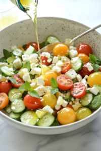 This image shows a large bowl filled with cherry tomatoes, cucumber slices, and crumbled feta cheese being gently tossed together, ensuring every bite is coated with the flavorful dressing.