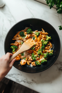 This image shows penne pasta, tender broccoli, and cooked chicken being mixed into the creamy sauce, ensuring every bite is coated with rich, flavorful goodness.