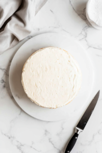 This image shows excess mirror glaze being trimmed from the edges of the cake to ensure a clean and professional presentation.