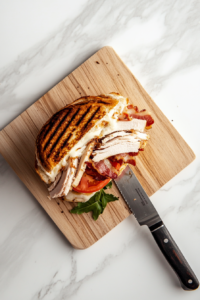 This image shows a turkey melt sandwich being sliced in half with a sharp knife, revealing its gooey melted cheese, layers of turkey, and crispy bread.