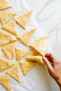 This image shows a sheet of crescent roll dough being unrolled on a flat surface, preparing it for cutting and wrapping.