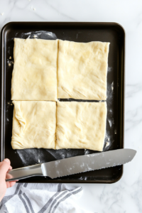 This image shows a sheet of crescent roll dough being unrolled and arranged on a flat surface, preparing for layering and filling to make cinnamon crescent twists.