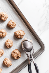 This image shows a cookie scoop being used to portion out banana bread cookie dough onto a prepared baking sheet for even baking.