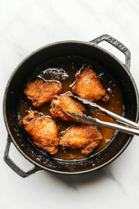 This image shows tongs carefully turning a piece of fried chicken in bubbling hot oil, ensuring even cooking and a crispy exterior.