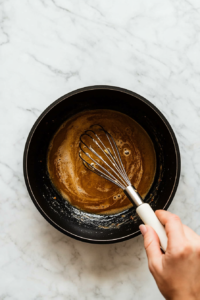 This image shows a hand whisking cubes of butter into the sauce, making it smooth and velvety.