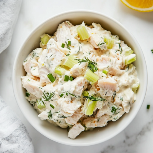This image shows A creamy and flavorful whitefish salad made with mayonnaise, sour cream, chopped celery, dill, and chives, perfect for serving with bagels and bread.