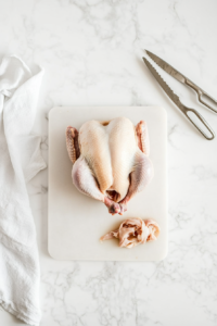 This image shows a whole chicken being placed into a large stockpot, ready to be simmered for a rich homemade broth.