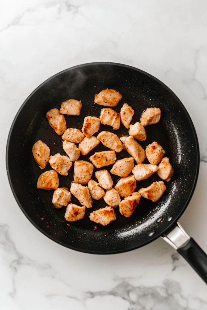 chicken-cooking-in-black-skillet-on-white-marble-cooktop