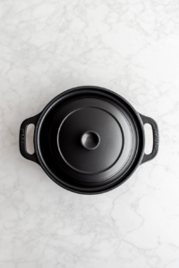 This image shows a black Dutch oven on low heat with its lid on, allowing the Kielbasa and Cabbage Soup to simmer gently, deepening its flavors.