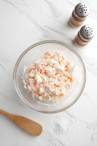 This image shows finely chopped fresh dill, Worcestershire sauce, and a sprinkle of salt and pepper being added to the crab dip, enhancing its depth of flavor and aromatic freshness.
