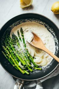 This image shows a creamy sauce being poured into a skillet with sautéed asparagus, creating a rich and flavorful base.