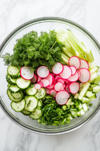 This image shows the freshly sliced cucumbers, radishes, and chopped celery being added to a bowl, ready to be tossed together for a refreshing salad.