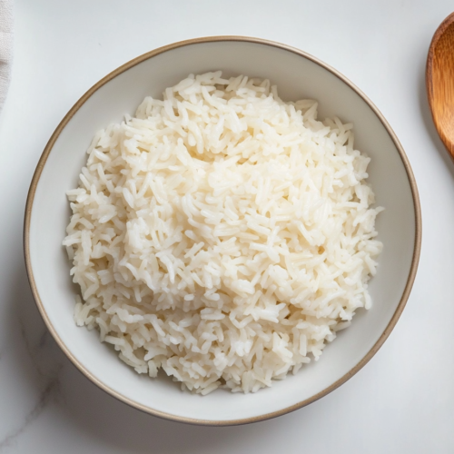 A bowl of freshly cooked Bomba rice, served in a round white bowl with a wooden spoon resting on the side, ready to be enjoyed.