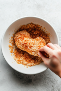 This image shows a chicken breast being dredged in flour, dipped in egg wash, and finally coated in crispy panko breadcrumbs for an ultra-crunchy texture.