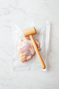 This image shows a chicken breast being pounded to an even thickness using a mallet, ensuring it cooks evenly and achieves the perfect crispy texture.