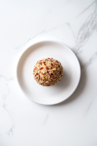 This image shows a beautifully plated cheese ball coated in pecans, served on a round white plate with crackers for dipping.