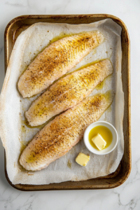 This image shows fresh tilapia fillets being generously seasoned with a blend of spices, preparing them for baking.