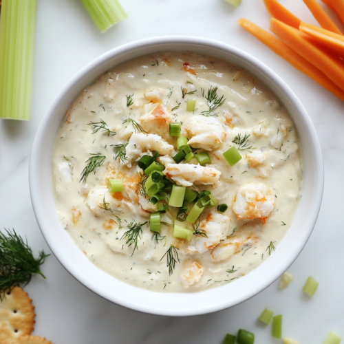 This image shows a creamy and smooth cold crab dip elegantly presented in a white bowl, topped with finely chopped fresh dill, highlighting its rich texture and vibrant flavors.