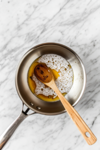 This image shows sugar and water being mixed together in a saucepan to create the sugar syrup that will infuse the Gulab Jamuns with sweetness.