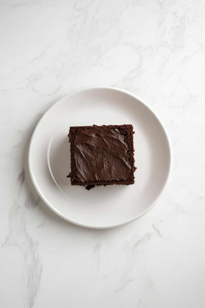 This image shows a square slice of devil’s food cake, piled high with chocolate frosting, creating a rich, indulgent dessert with a deep, chocolatey flavor.