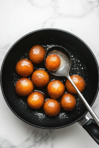 This image shows the fried Gulab Jamuns being lifted from the hot ghee and drained to remove excess oil before adding to the syrup.
