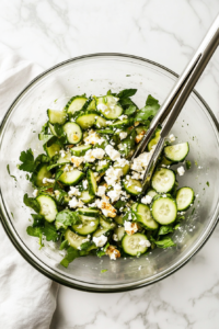 This image shows the dressing being drizzled over the cucumber feta salad, followed by tossing the ingredients to ensure they are evenly coated with the flavorful dressing.