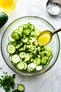 This image shows lime juice and olive oil being added to the cucumber avocado salad, along with a sprinkle of salt and pepper to enhance the flavors.
