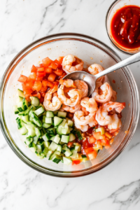 This image shows a smooth, flavorful dressing being poured over the shrimp cocktail mixture, enhancing its bright and zesty taste.