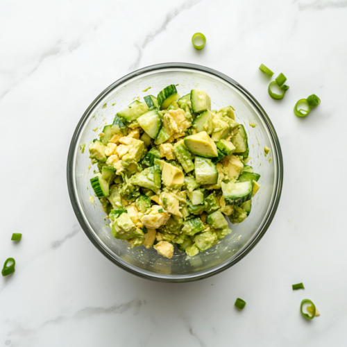 This image shows a vibrant cucumber avocado salad in a glass bowl, featuring creamy avocado, crisp cucumber, and chopped green onions, tossed with lime juice and olive oil for a refreshing and zesty flavor.