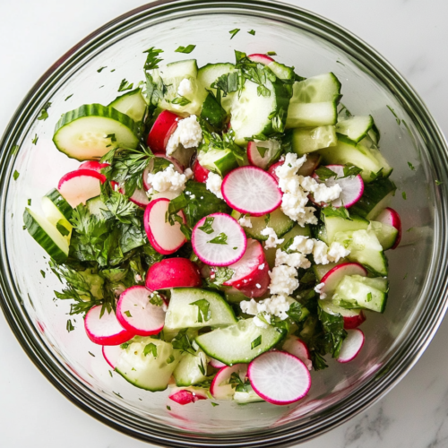 This image shows a fresh cucumber radish salad with vibrant slices of cucumber and radish, topped with crumbled cheese, creating a refreshing and flavorful dish.