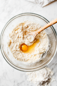 This image shows a mixing bowl filled with freshly made noodle dough, being combined and kneaded to create homemade, tender egg noodles for the dish.