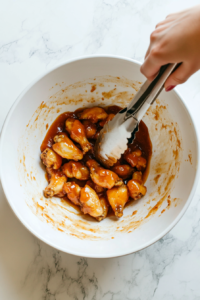 This image shows crispy chicken wings being tossed in a bowl of homemade mango habanero sauce, evenly coating each wing.
