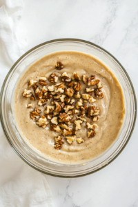 This image shows a spatula gently folding chopped walnuts into the banana bread batter, adding texture and nutty flavor to the loaf. This step is optional for those who love a crunchy bite.