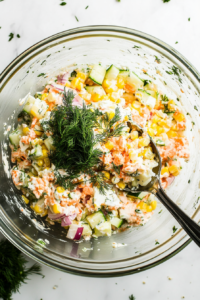 This image shows finely chopped fresh dill and parsley being stirred into the Russian Crab Salad, adding a burst of color, freshness, and an aromatic touch to the creamy dish.