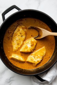 This image shows fresh fish pieces gently simmering in the rich curry sauce, absorbing the coconut-infused flavors for a perfectly tender bite.